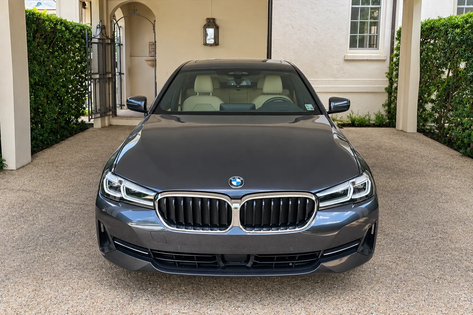 Front view of a gray BMW sedan with installed windshield in a covered driveway.