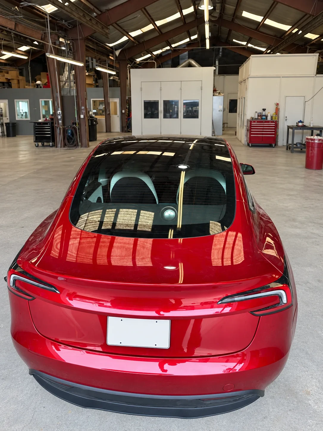 Rear view of a red Tesla with installed rear glass in a workshop.